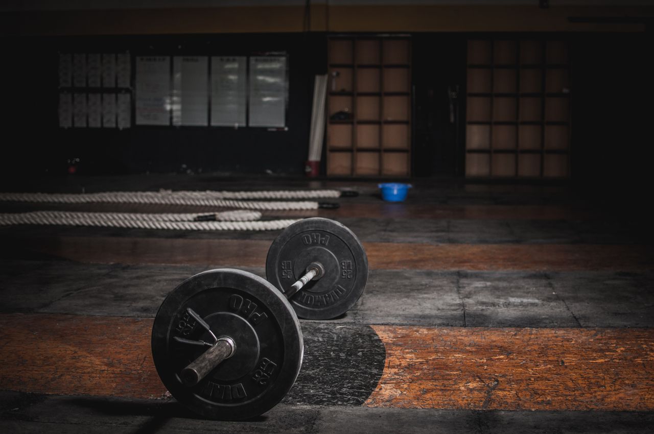 Strona główna A lone barbell rests in an empty, dimly lit gym, emphasizing strength and solitude.
