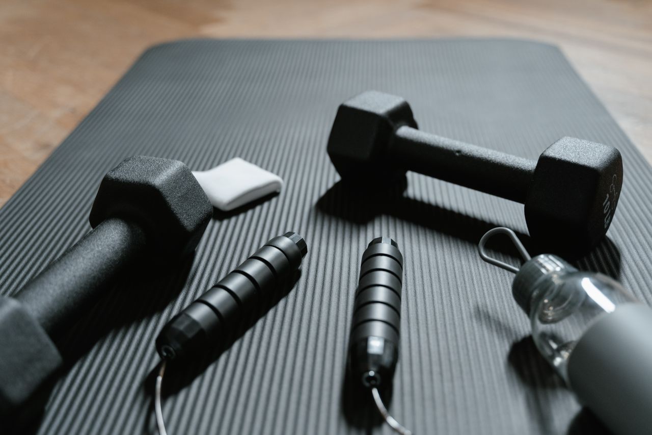 Strona główna Close-up of dumbbells, jump rope, and water bottle on a yoga mat, ideal for home fitness routines.